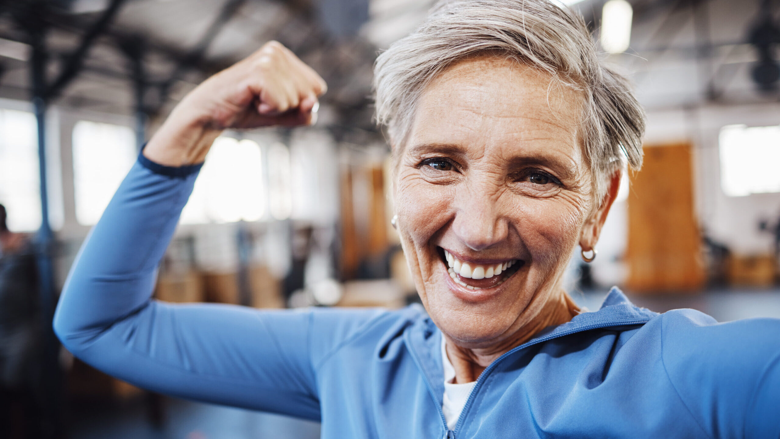 Over 50 senior woman flexing in gym after personal training session.