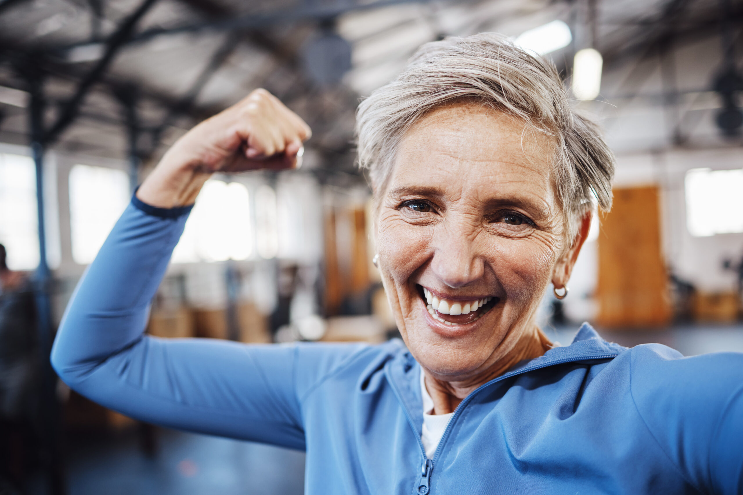 Over 50 senior woman flexing in gym after personal training session.